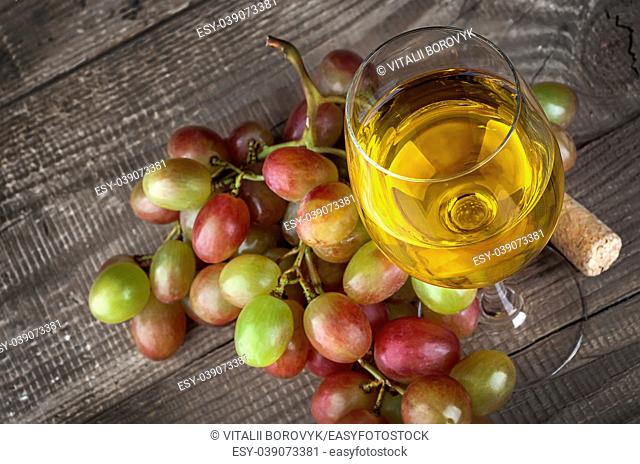 Glass of white wine with a cluster of grapes on wooden table background, top view