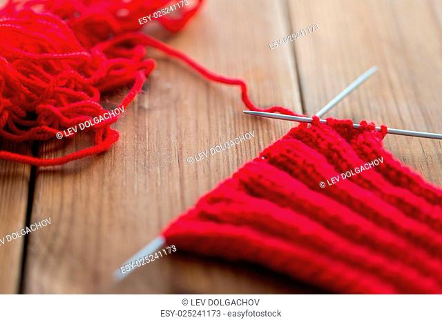 handicraft and needlework concept - hand-knitted item with knitting needles on wood