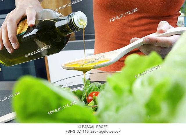 Mid section view of a woman pouring olive oil into a wooden spoon