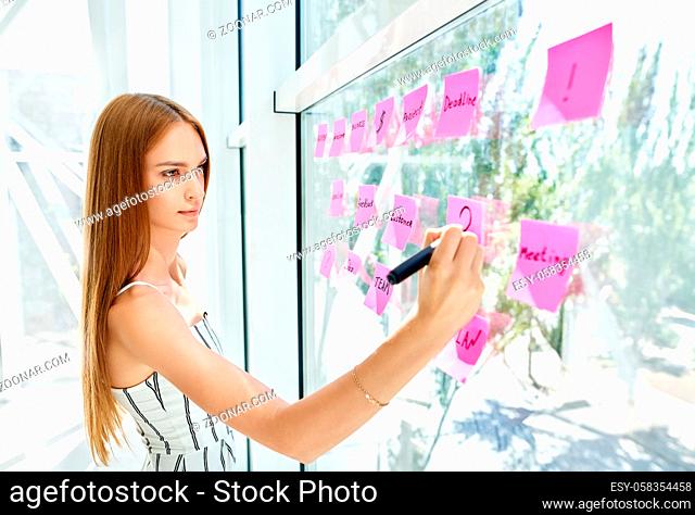 Attractive concentrated business woman using sticky notes to write and share ideas in creative office. business, people, teamwork and planning concept