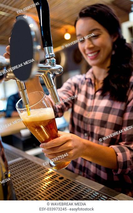 Pretty barmaid pouring beer from tap in glass