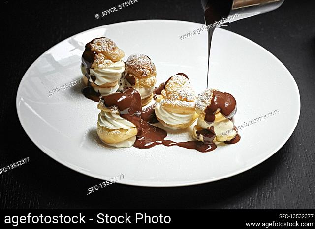 Profiteroles being drizzled with chocolate sauce