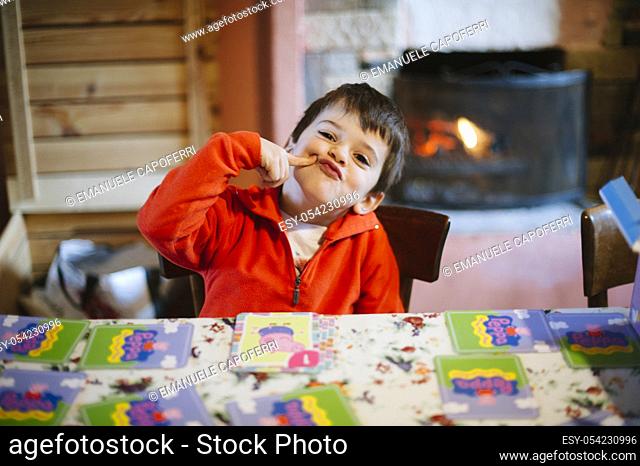 Portrait of little boy sitting at the table while making grimaces