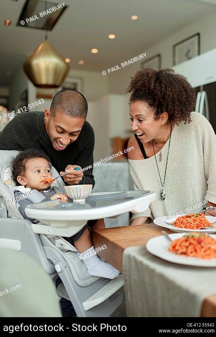 Happy couple feeding baby daughter in high chair