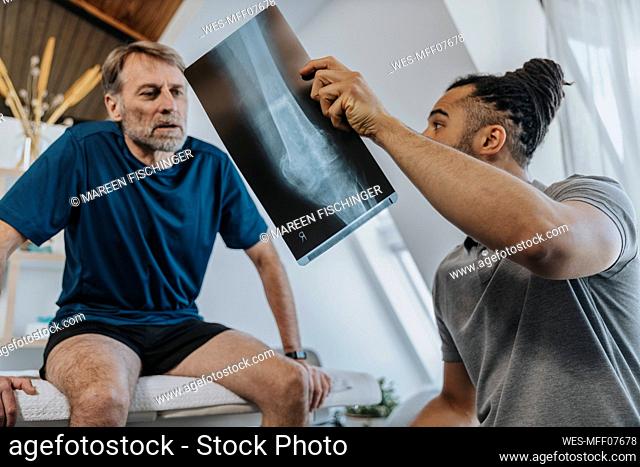 Physiotherapist discussing x-ray image of knee with male patient