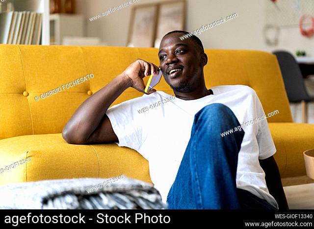 Man talking on mobile phone while sitting by sofa at home