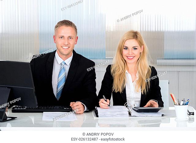 Portrait of smiling male and female accountants calculating finance at desk in office