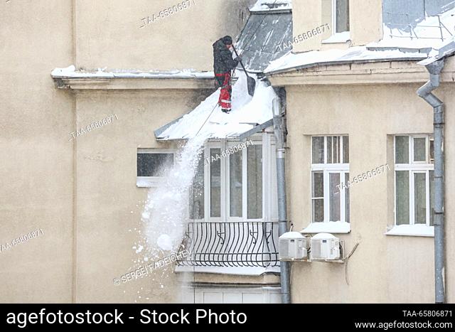 RUSSIA, MOSCOW - DECEMBER 16, 2023: A worker clears snow from the roof of a residential building after a heavy snowstorm in winter