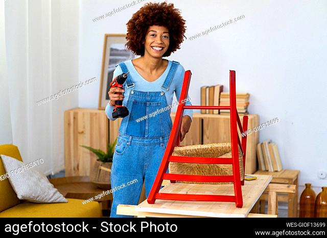 Smiling redhead woman with electric screwdriver standing at table