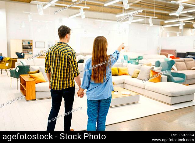Happy couple choosing furniture in store showroom. Man and woman looking samples for bedroom in shop, husband and wife buys goods for modern home interior