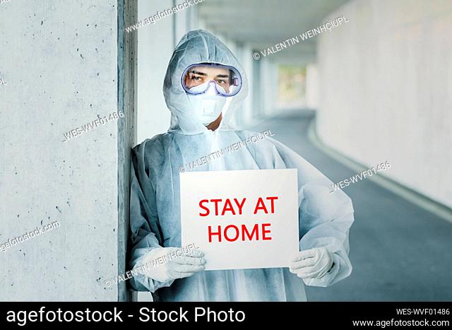 Portrait of man wearing protective clothing holding a 'stay at home' sign