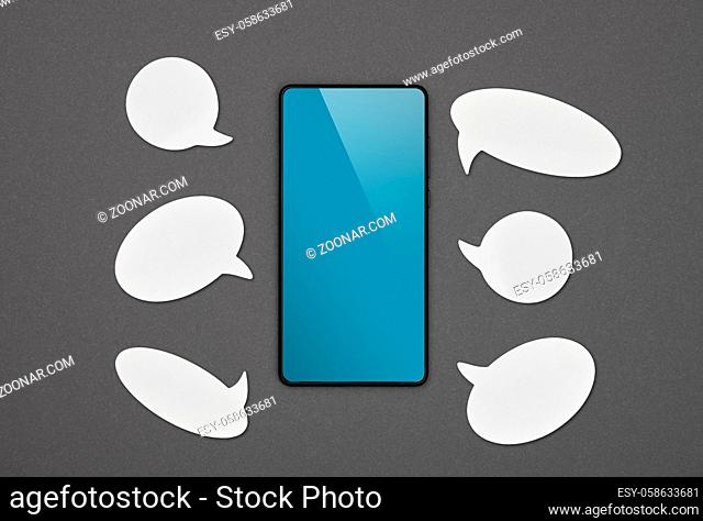 Close up one black smartphone with blank blue screen and white empty copy space callouts over grey paper background, flat lay, directly above