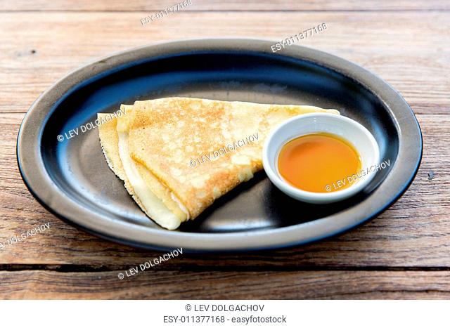 food, morning and eating concept - close up of plate with pancakes and honey or jam on table