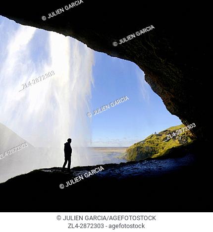 Iceland, Sudurland region, Seljalandsfoss waterfall, silhouette of man on a path passing behind the waterfall