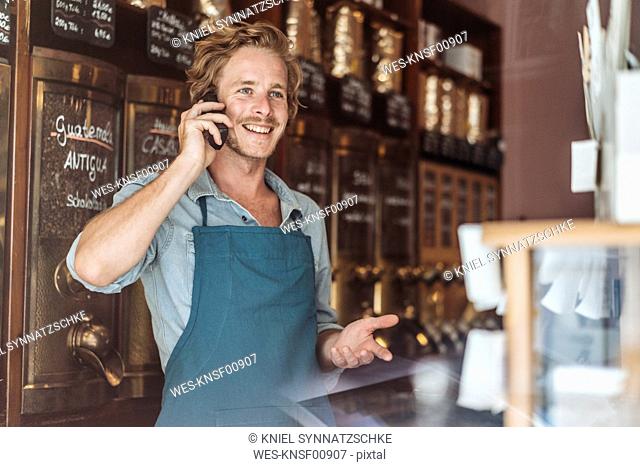 Smiling coffee roaster in his shop on the phone