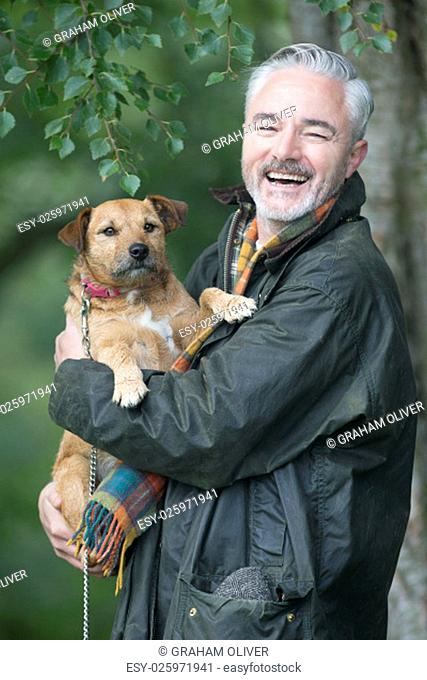 Portrait of a man holding his dog in a field. He is smiling for the camera
