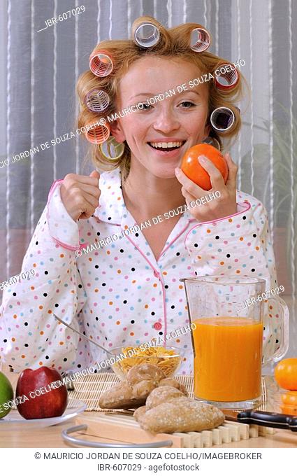 Redheaded woman wearing pajamas with curlers in her hair eating breakfast
