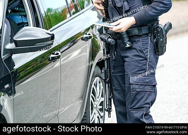 19 May 2021, Schleswig-Holstein, Dänischenhagen: A policeman carrying a submachine gun examines a car on the street in front of a house where two dead people...