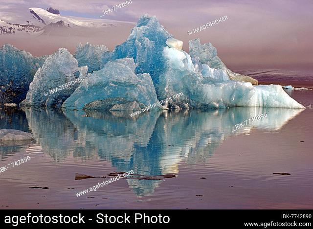 Blue iceberg reflected in the water, mountains rising out of the mist, Jökulsarlon, glacier lagoon, Scandinavia, Iceland, Europe