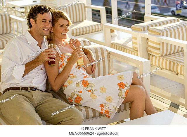 Couple is sitting arm in arm with drinks on cafe terrace in summery clothes