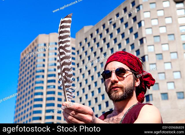 An eagle feather is viewed close up, in the hand of a nonconformist bearded male. Creative person seeks inspiration downtown