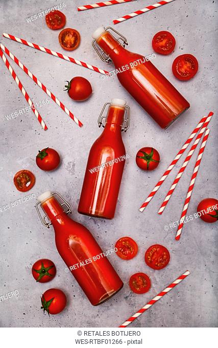 Homemade tomato juice in swing top bottles, straws and tomatoes on grey ground