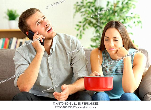 Upset couple sitting in a couch in the living room and calling insurance for home leaks