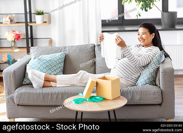happy pregnant woman with baby's bodysuit at home