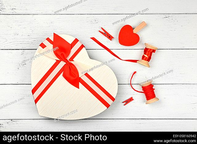 Packing Valentine heart shaped gift box with ribbon chiffon bow over white wooden table background, close up flat lay, elevated top view, directly above
