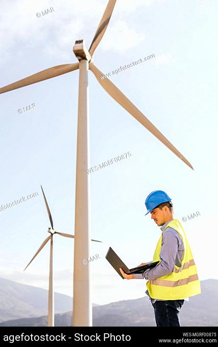 Engineer working on laptop in front of wind turbines