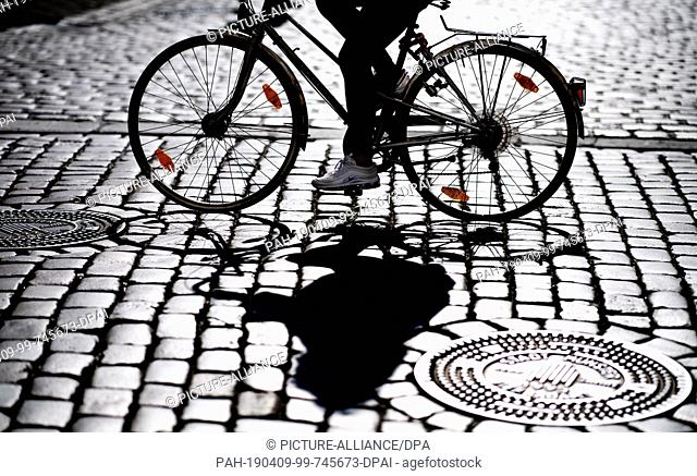 09 April 2019, North Rhine-Westphalia, Münster: A cyclist rides on the Prinzipalmarkt in Münster and casts a shadow on the cobblestones