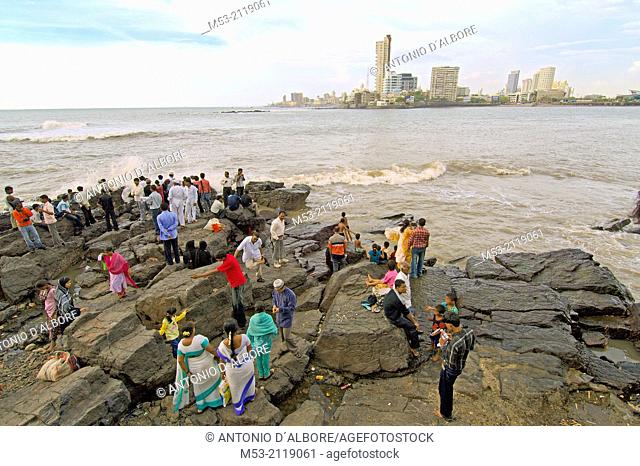 indian people enjoy fresh breeze from arabian sea on a rocky area outside the haji ali's mosque and tomb in worli district. mumbay. maharashtra. india