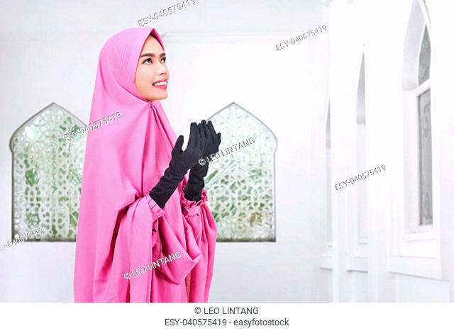 Young asian muslim woman in veil praying on the mosque