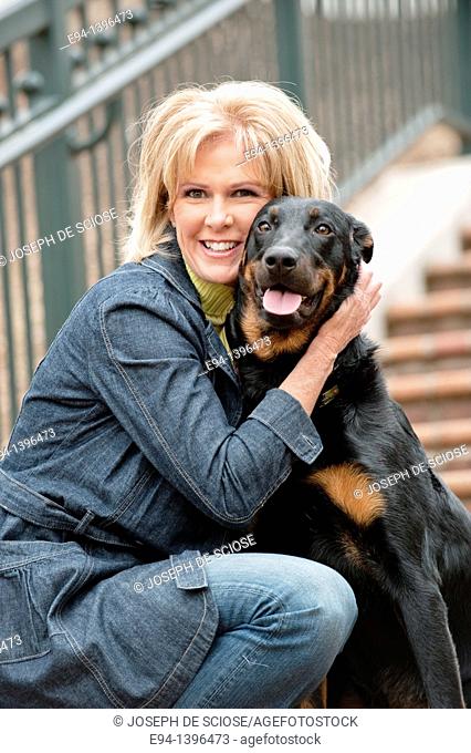 Fifty year old blond woman hugging a Doberman Pinscher on a stairway in a park