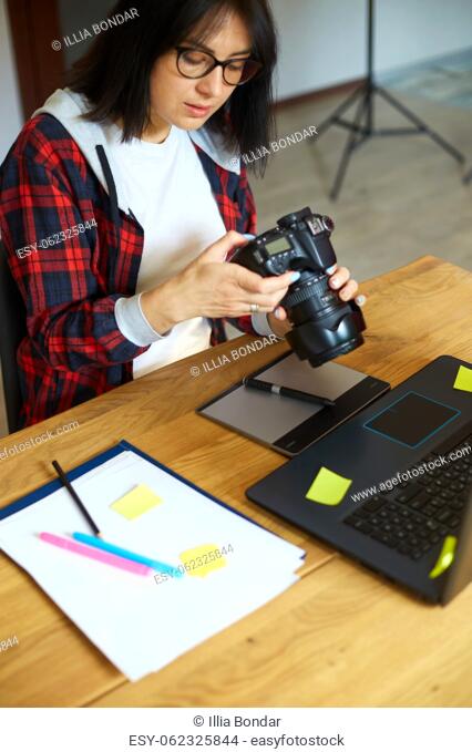 Photographer female working in a creative office holding camera, at desk and retouch photo on laptop, Retoucher workplace in photo studio