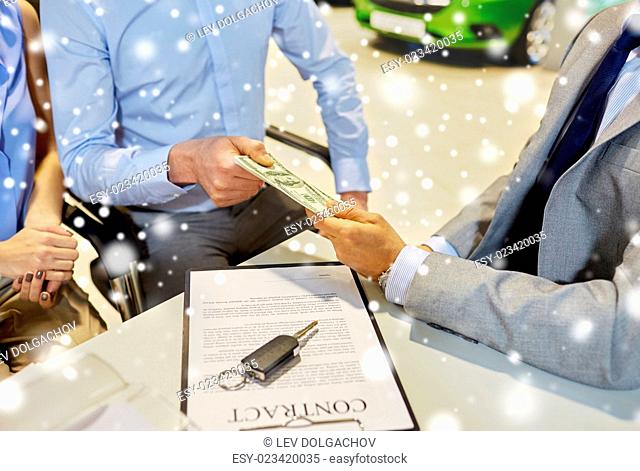 auto business, sale and people concept - close up of customers giving money to dealer and buying car in auto show or salon over snow effect