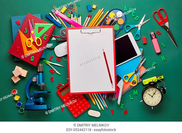 Red clipboard with blank sheet, computer tablet, microscope and stationery accessories on green background. Top view, copy space
