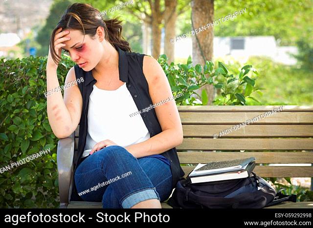 Sad Bruised and Battered Young Woman Sitting on Bench Outside at a Park