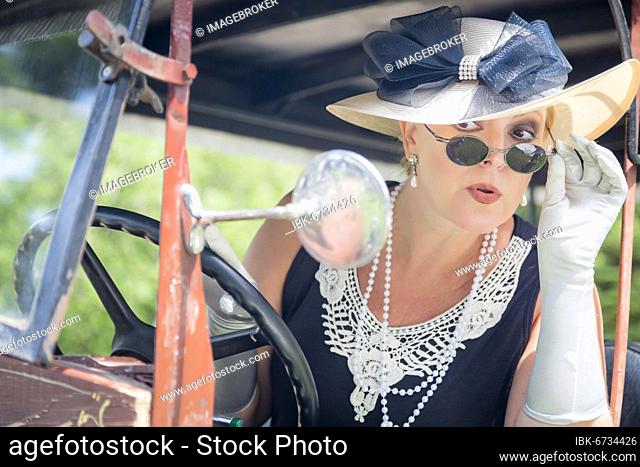 Attractive young woman in twenties outfit checking makeup in antique automobile