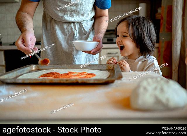 Cheerful boy with father preparing pizza at home