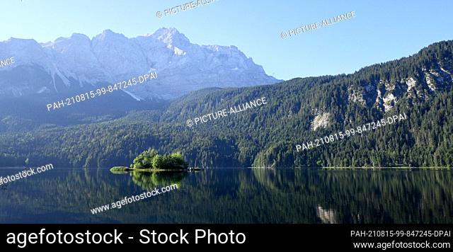 15 August 2021, Bavaria, Grainau: A woman paddles across the morning Eibsee, in the background in the middle the Zugspitze