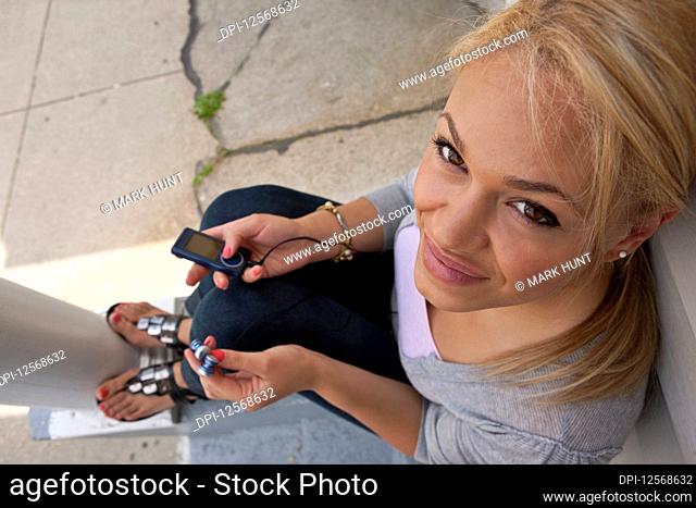 Young woman looks up at the camera with a smile while holding a portable music player with earphones