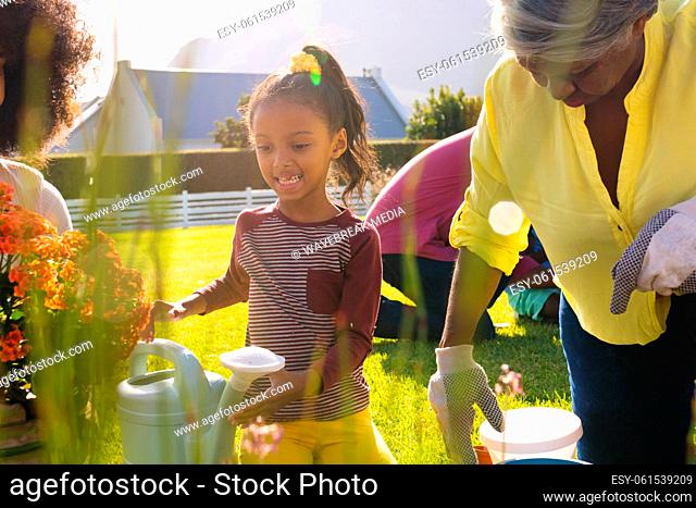 Multiracial smiling girl with mother and grandmother planting in yard during sunny day