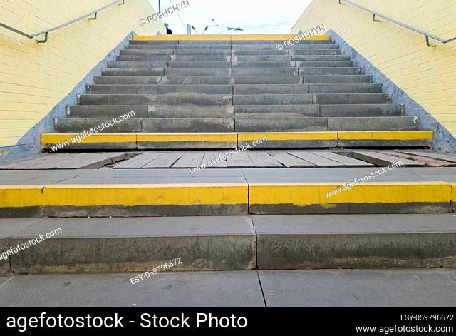 Empty yellow underground pedestrian crossing. Tunnel and daylight at the end. Steps to the top at the pedestrian crossing