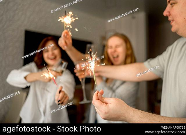 Cheerful friends having fun with sparklers at home