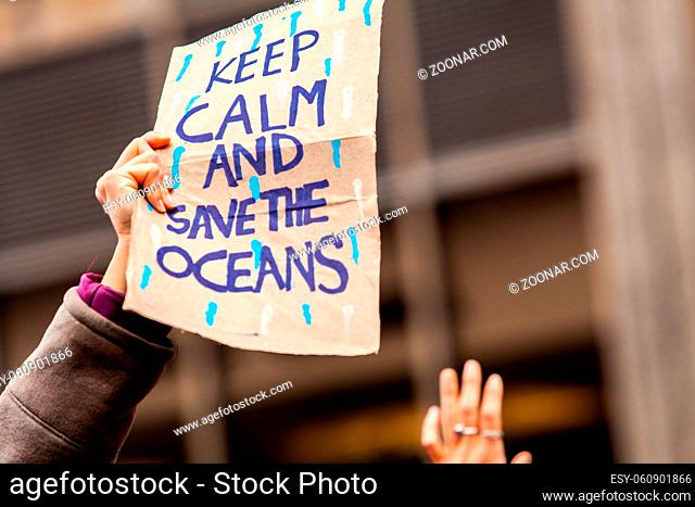 A closeup view of a cardboard sign saying keep calm and save the oceans during a climate change rally in a city center. Environmental protest
