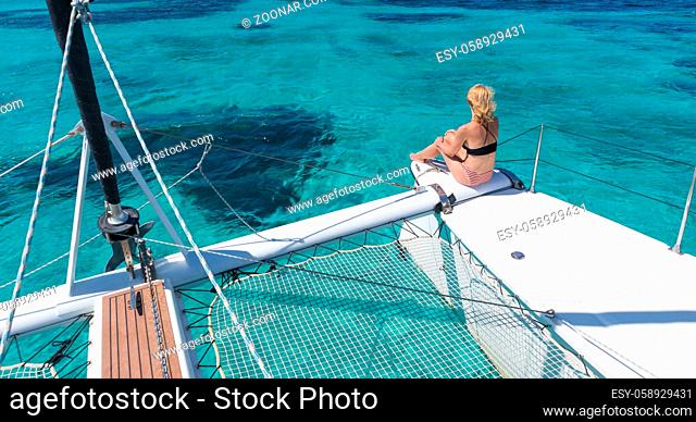 Woman in bikini tanning and relaxing on a summer sailin cruise, sitting on a luxury catamaran in picture perfect turquoise blue lagoon near Spargi island in...