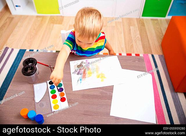 Little child drawing on the paper. Boy sitting on the chair at table with paints