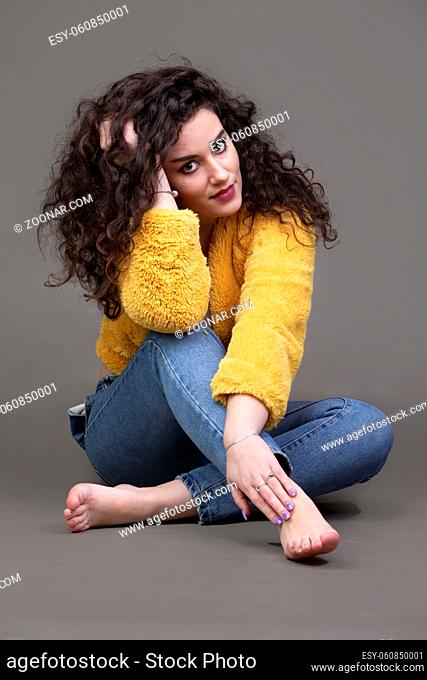 Beautiful brunette girl with curly hair in jeans on a gray background