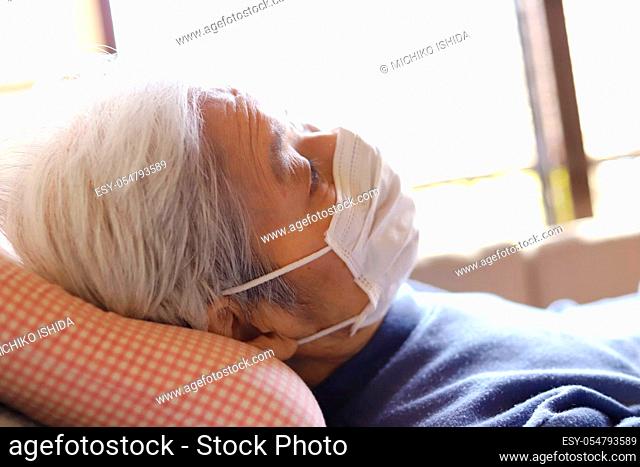 Senior lady lying on the nursing care bed with the surgical mask for virus protection
